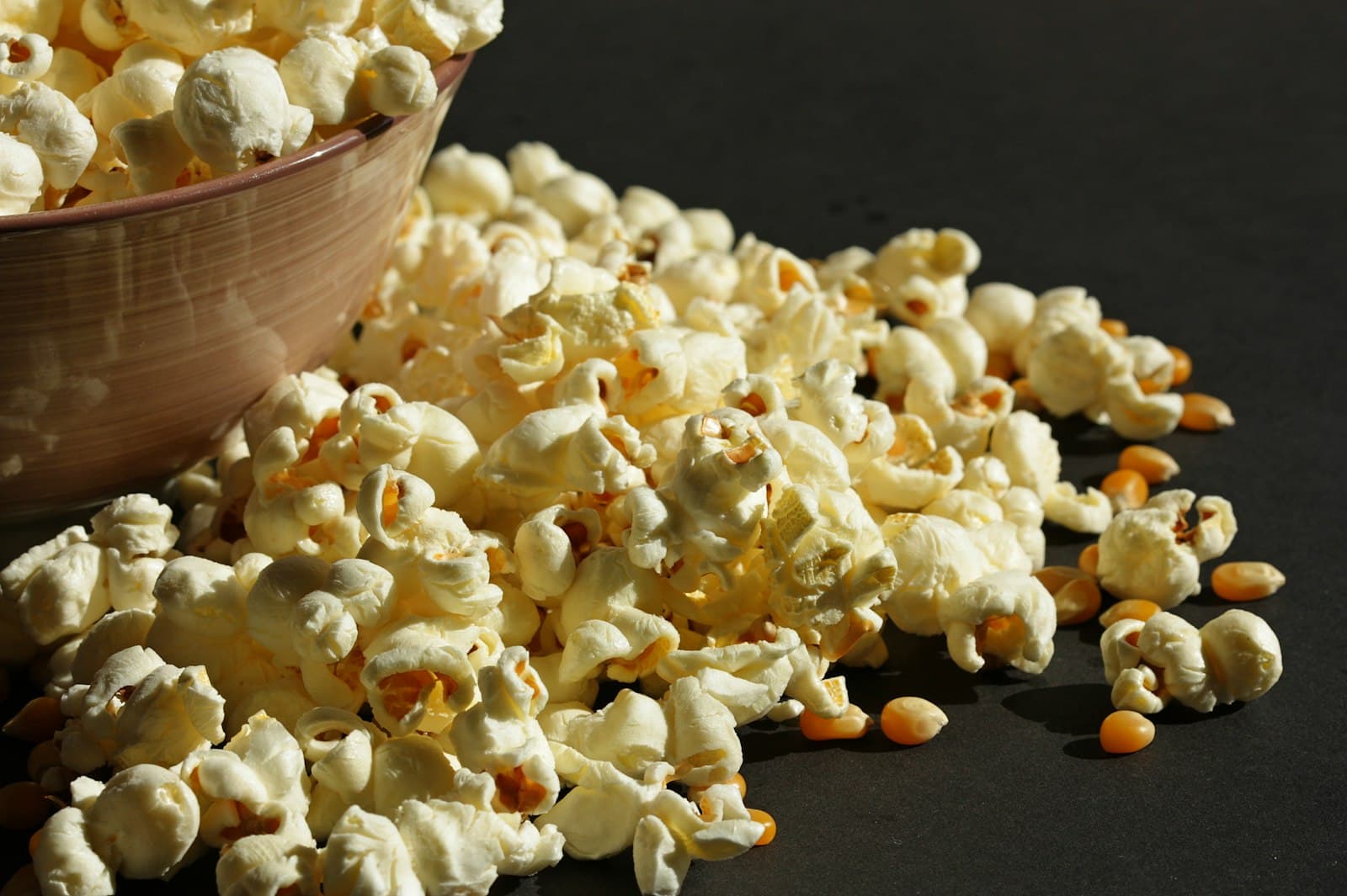 Popcorn spilling from a bowl with raw kernels
